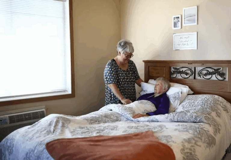 senior female laying in a bed with female at her bedside