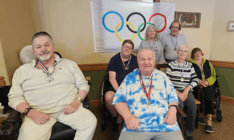 a group of seniors waiting to play olympic games sitting on chairs with the olympics symbol in the background