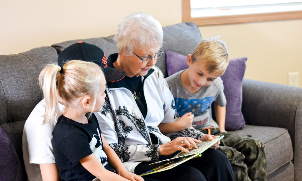 senior woman sitting on couch with kids looking at a book of photos
